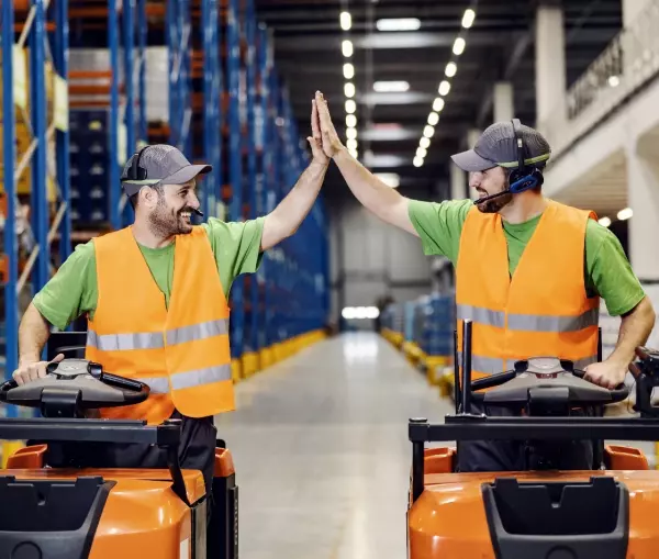 Twee werknemers met fluovest op een orderpicktruck geven elkaar een high five